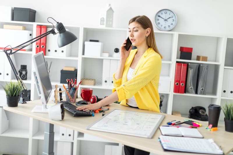 Una ragazza sta stando vicino ad una tavola, sta parlando sul telefono e sta lavorando con un computer Prima della ragazza sulla fotografia stock