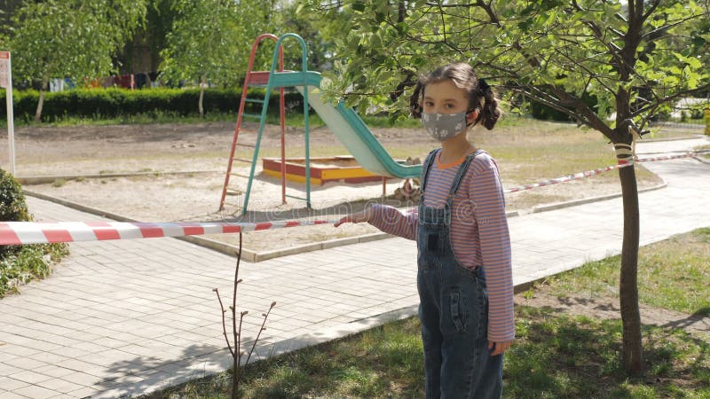 Una ragazza triste cammina vicino a un parco giochi chiuso a causa della quarantena. il parco giochi per bambini è recintato con u