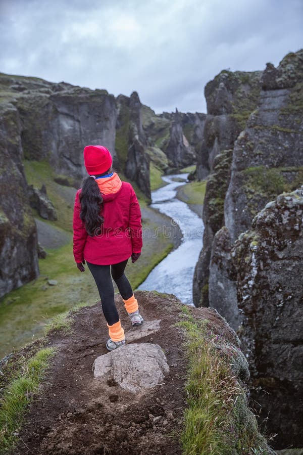 Una ragazza in un rivestimento rosso sta sull'orlo di una gola profonda L'Islanda contenuta immagine fotografia stock Una ragazza in un rivestimento rosso sta sull'orlo di una gola profonda L'Islanda contenuta immagine fotografia stock
