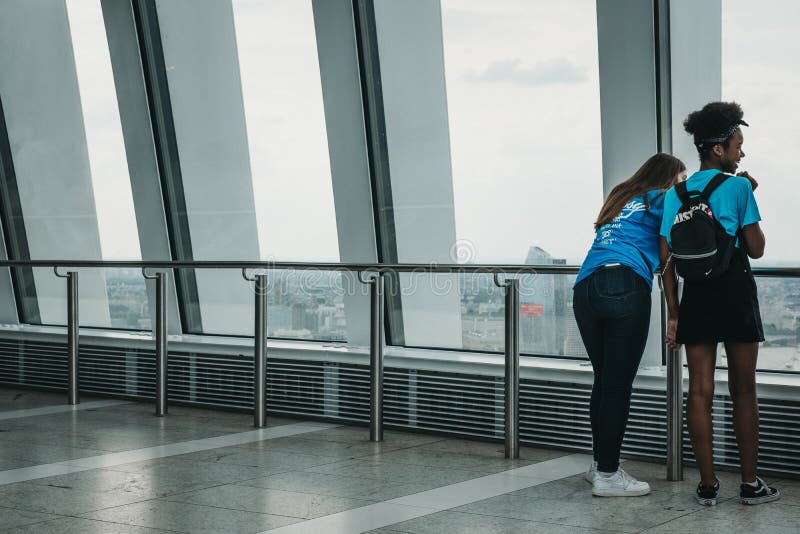 Una retrovisione di due giovani donne che godono della vista della città dal cielo fa il giardinaggio, Londra, Regno Unito immagini stock Una retrovisione di due giovani donne che godono della vista della città dal cielo fa il giardinaggio, Londra, Regno Unito immagini stock