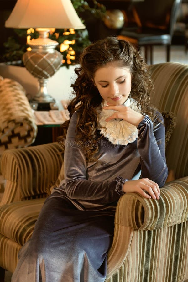 una señora joven medieval se sienta en una silla antigua acogedora del sofá en ojos abatidos pasados de moda de un interior modes fotografía de archivo una señora joven medieval se sienta en una silla antigua acogedora del sofá en ojos abatidos pasados de moda de un interior modes fotografía de archivo