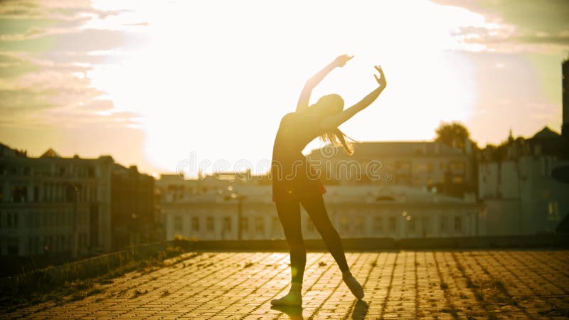 Una siluetta della ballerina della giovane donna nella condizione del vestito nella posa graziosa sul tetto su un fondo di modern fotografia stock Una siluetta della ballerina della giovane donna nella condizione del vestito nella posa graziosa sul tetto su un fondo di modern fotografia stock