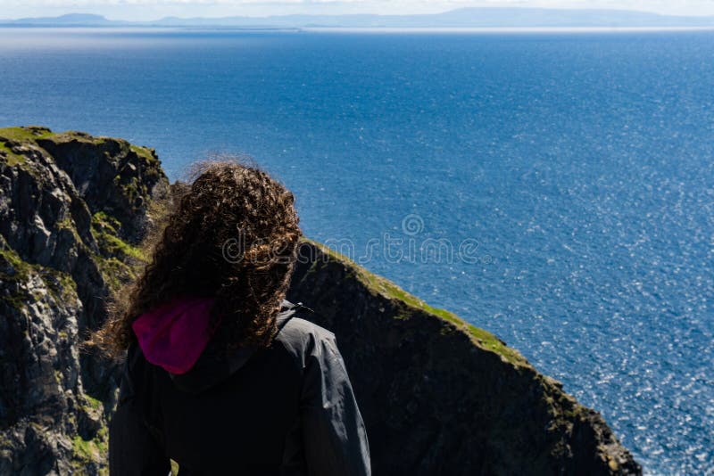 Una situación de la mujer al borde de un alto acantilado irlandés con el océano en el fondo fotografía de archivo Una situación de la mujer al borde de un alto acantilado irlandés con el océano en el fondo fotografía de archivo