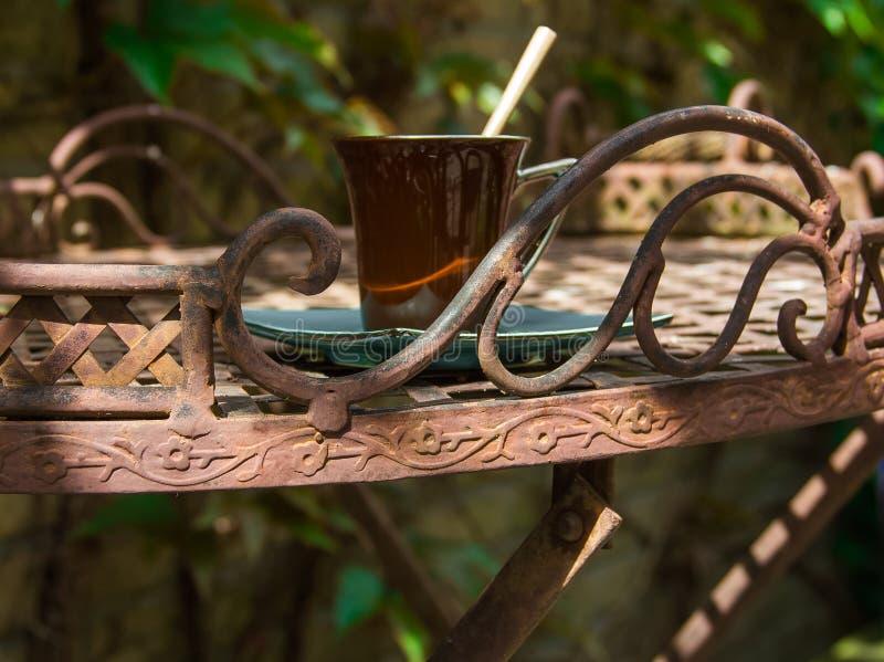 Una taza de café en la tabla decorativa forjada en jardín fotografía de archivo libre de regalías Una taza de café en la tabla decorativa forjada en jardín fotografía de archivo libre de regalías