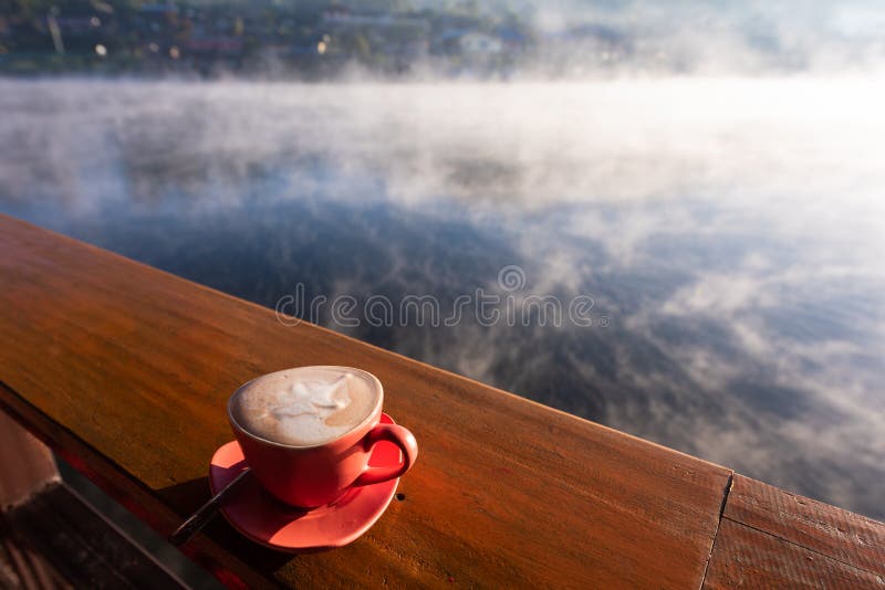 Una taza de café en la tabla de madera con vapor sobre el lago en el pueblo tailandés de Rak imagen de archivo libre de regalías Una taza de café en la tabla de madera con vapor sobre el lago en el pueblo tailandés de Rak imagen de archivo libre de regalías