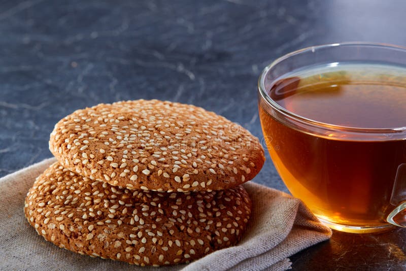 Una taza de cristal de té negro con las galletas del sesam en un fondo de mármol grisáceo oscuro, profundidad del campo baja fotos de archivo Una taza de cristal de té negro con las galletas del sesam en un fondo de mármol grisáceo oscuro, profundidad del campo baja fotos de archivo