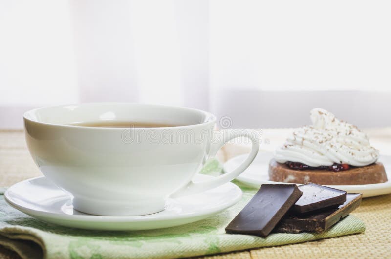Una taza de té, una torta de chocolate con crema de la clara de huevo y pedazos de chocolate imagen de archivo libre de regalías Una taza de té, una torta de chocolate con crema de la clara de huevo y pedazos de chocolate imagen de archivo libre de regalías