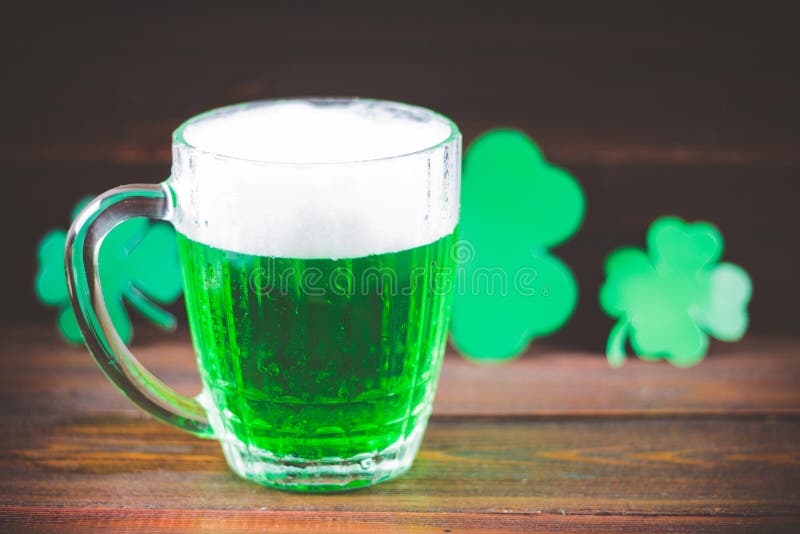 Una tazza di birra verde sulla tavola Fogli del trifoglio bianco Petto di oro, mucchio delle monete Giorno di s di StPatrick ' immagine stock Una tazza di birra verde sulla tavola Fogli del trifoglio bianco Petto di oro, mucchio delle monete Giorno di s di StPatrick ' immagine stock