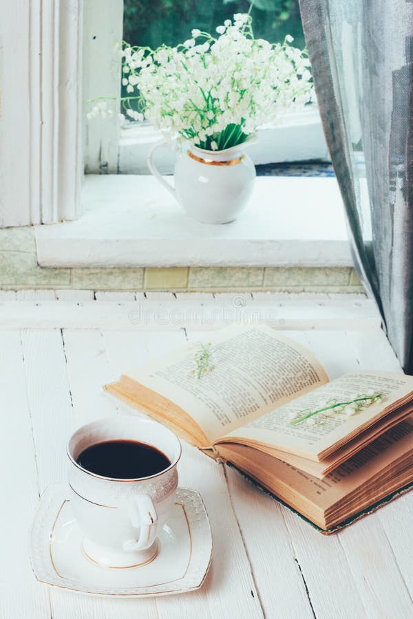 Una tazza di caffè nero e di un libro aperto su una retro tavola d'annata di legno bianca e di un mazzo dei fiori del mughetto su fotografia stock libera da diritti Una tazza di caffè nero e di un libro aperto su una retro tavola d'annata di legno bianca e di un mazzo dei fiori del mughetto su fotografia stock libera da diritti