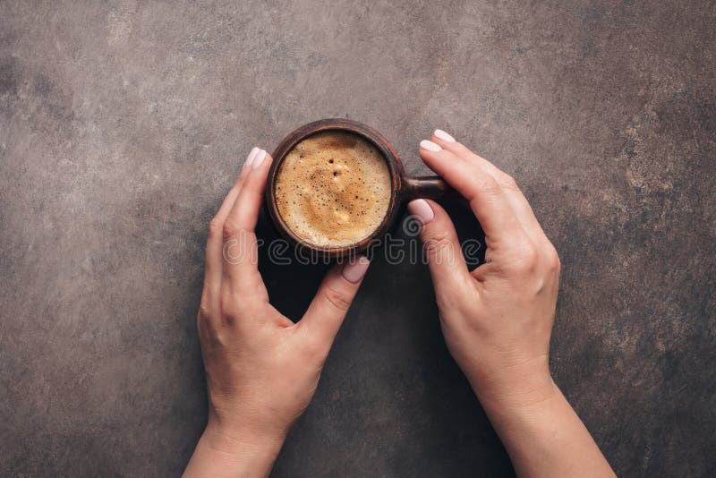 Una tazza di delizioso caffè cappuccino in mani femminili, fondo rustico scuro, vista dall'alto immagine stock Una tazza di delizioso caffè cappuccino in mani femminili, fondo rustico scuro, vista dall'alto immagine stock