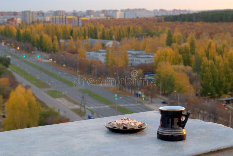 Una tazza nera con caffè e un piattino con pezzettini di cioccolato sul parapetto del tetto su uno sfondo sfuocato fotografia stock Una tazza nera con caffè e un piattino con pezzettini di cioccolato sul parapetto del tetto su uno sfondo sfuocato fotografia stock