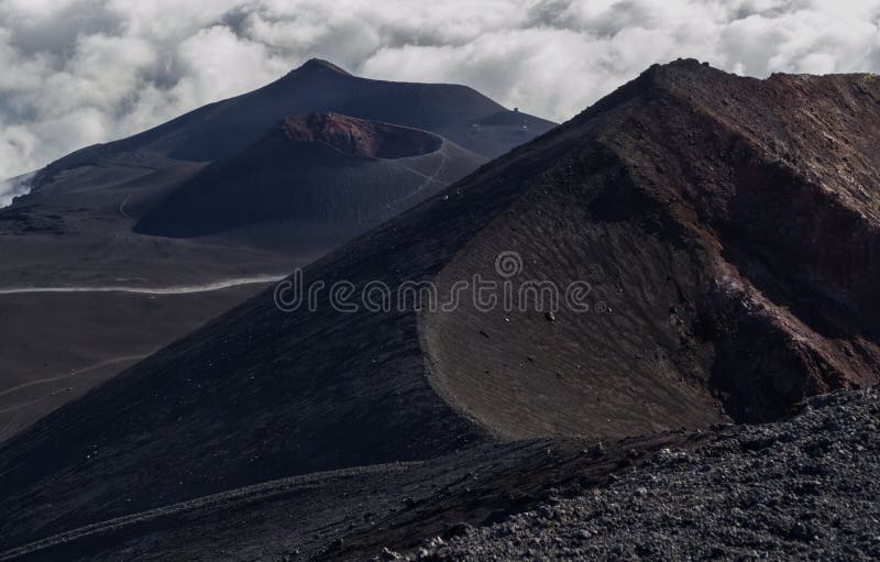 Una trayectoria en la lava negra entre los cráteres extintos en la cima del volcán del Etna entre las nubes foto de archivo Una trayectoria en la lava negra entre los cráteres extintos en la cima del volcán del Etna entre las nubes foto de archivo