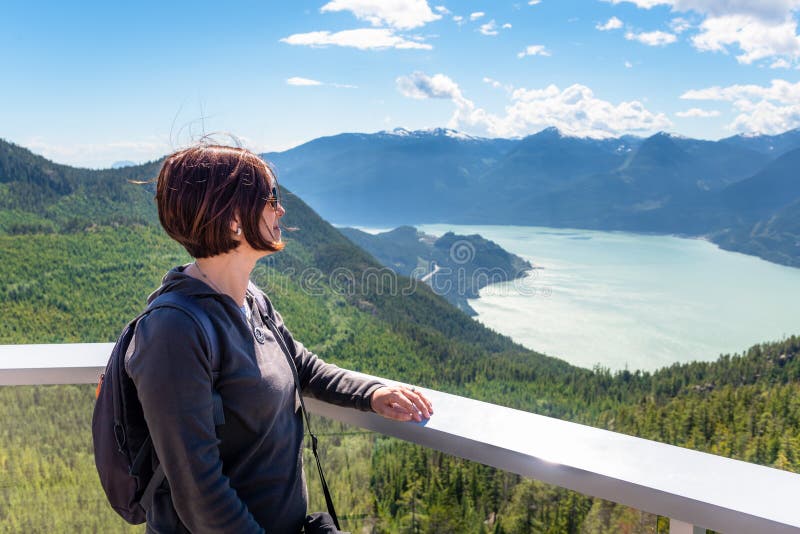 Una turista che ammira il paesaggio dalla cima di una montagna durante una soleggiata giornata estiva fotografia stock Una turista che ammira il paesaggio dalla cima di una montagna durante una soleggiata giornata estiva fotografia stock