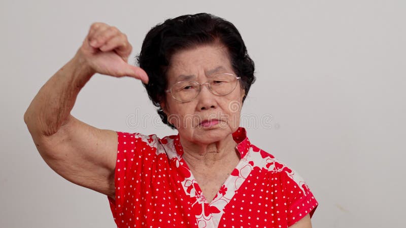 Una vecchia donna seria e scontenta dell'Asia che mostra il pollice in basso sullo sfondo bianco e guarda il segno negativo della