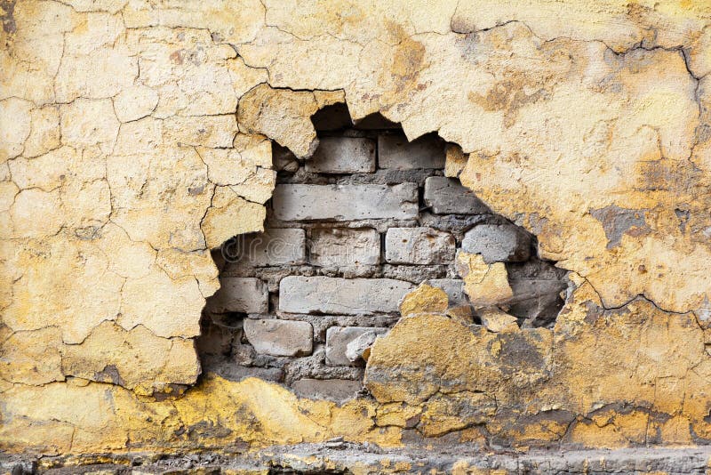 Una pared de ladrillo gris antiguo con grietas y un fragmento en ruinas de estuco amarillo. La textura del fondo para la reparació