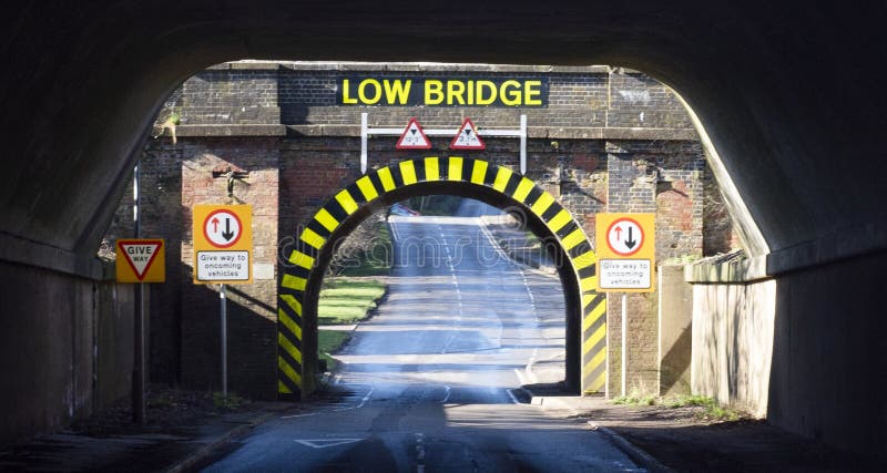 Una vista de un túnel de un solo carril con franjas de advertencia y letras amarillas y negras que indica un puente bajo