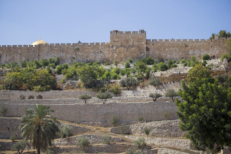 An interesting view of the ancient stone walls surrounded by trees and the Golden Gate of Jerusalem against the blue cloudless sky. An interesting view of the ancient stone walls surrounded by trees and the Golden Gate of Jerusalem against the blue cloudless sky