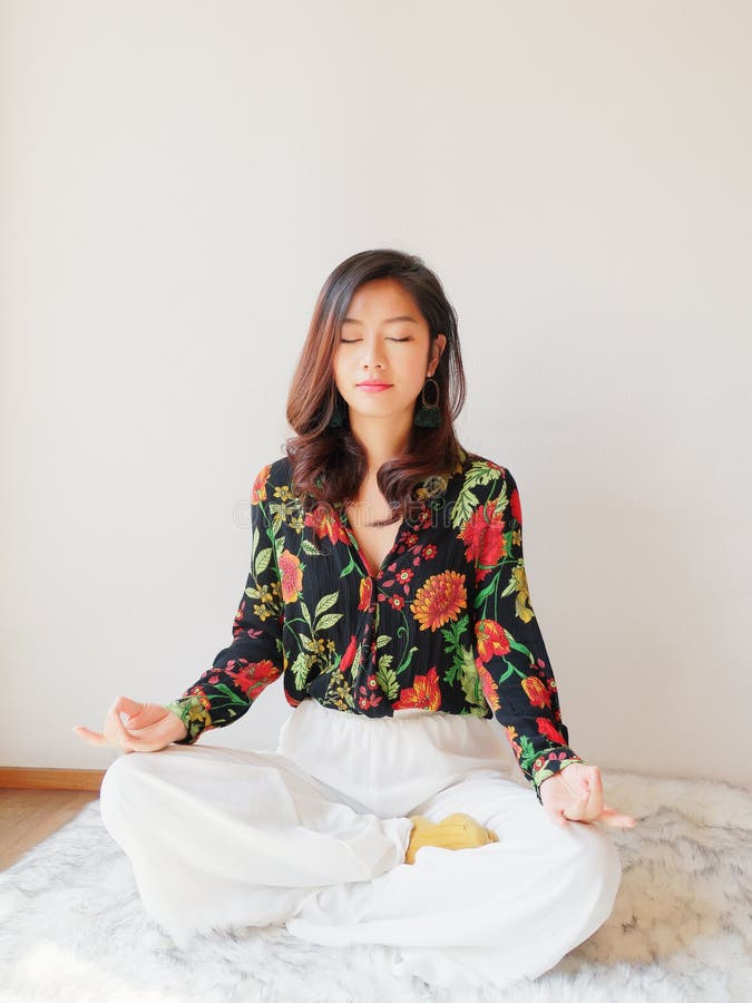Una yoga practicante china bonita de la mujer joven en casa, sentándose en piso con el amortiguador peludo cerca de puerta de cri fotografía de archivo Una yoga practicante china bonita de la mujer joven en casa, sentándose en piso con el amortiguador peludo cerca de puerta de cri fotografía de archivo