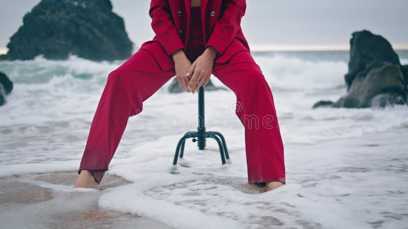 Unbekannte Frau sitzt am Strand und trägt einen roten Stilanzug.
