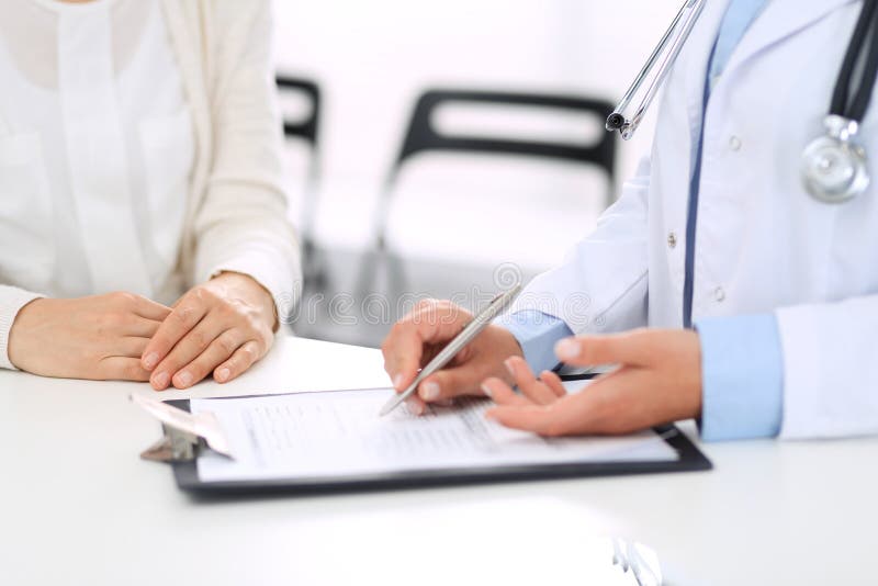 Unbekannte Ärztin und weiblicher Patient, die etwas bei der Stellung nahe Aufnahmeschreibtisch im Notkrankenhaus bespricht lizenzfreie stockbilder Unbekannte Ärztin und weiblicher Patient, die etwas bei der Stellung nahe Aufnahmeschreibtisch im Notkrankenhaus bespricht lizenzfreie stockbilder