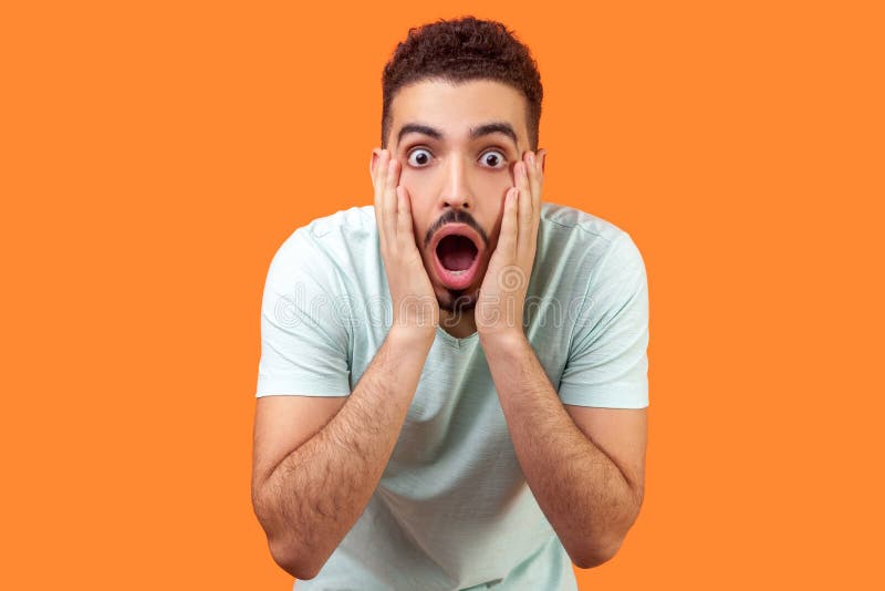 Unbelievable shocking news! Portrait of stunned brunette man keeping mouth wide open in amazement 突显在橙色背景中 免版税库存照片