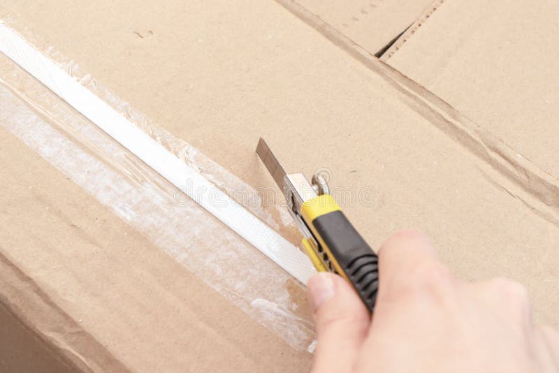 Unboxing ένα κουτί από χαρτόνι με τα νέα έπιπλα με το μαχαίρι κατασκευής ή γραφείων - που κινείται προς το καινούργιο σπίτι και π στοκ φωτογραφία Unboxing ένα κουτί από χαρτόνι με τα νέα έπιπλα με το μαχαίρι κατασκευής ή γραφείων - που κινείται προς το καινούργιο σπίτι και π στοκ φωτογραφία