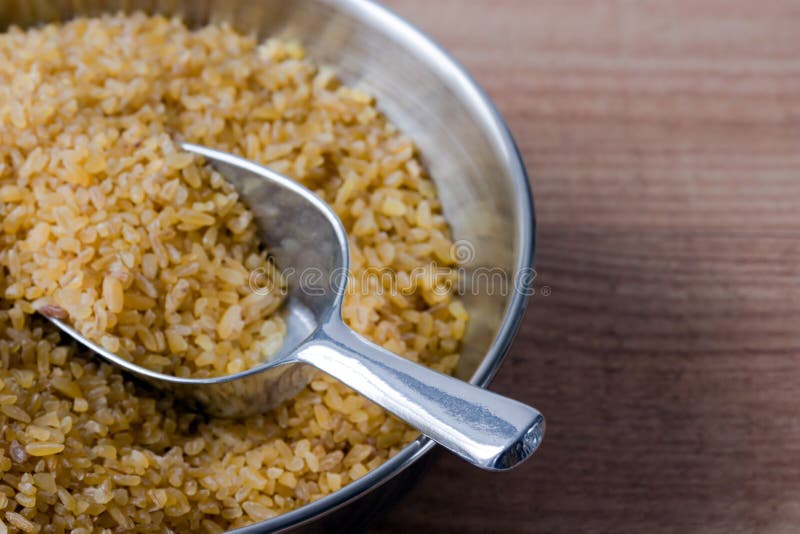 Bowl with uncooked bulgur on a wooden board.