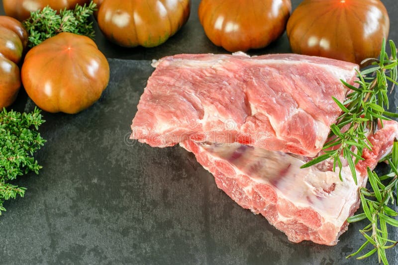 Uncooked fresh pork ribs prepared for cooking with tomatoes and fresh herbs on the black kitchen board. Healthy organic food stock images Uncooked fresh pork ribs prepared for cooking with tomatoes and fresh herbs on the black kitchen board. Healthy organic food stock images