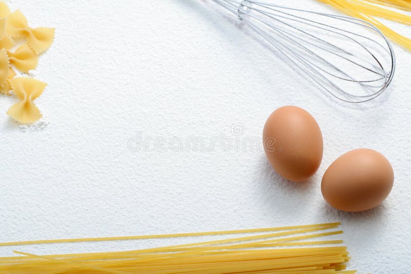 Uncooked macaroni, whisk and eggs on wheat flour