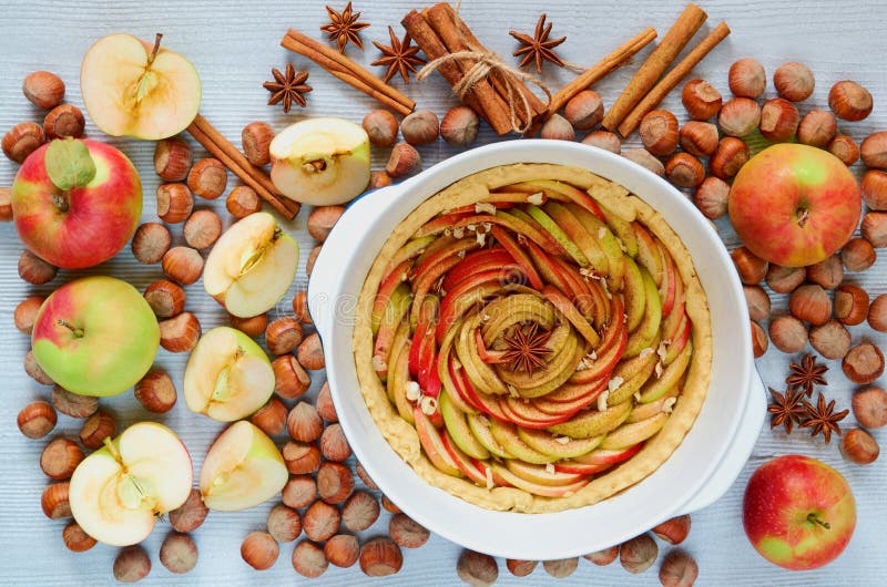 Uncooked tart tatin in the baking dish decorated with fresh sliced apples, hazelnuts, cinnamon sticks, anise stars. Homemade pie