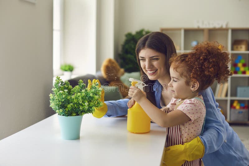 Lovely little girl helping her mother water houseplant at home, copy space text. Happy parent and child doing domestic chores together. Lovely little girl helping her mother water houseplant at home, copy space text. Happy parent and child doing domestic chores together