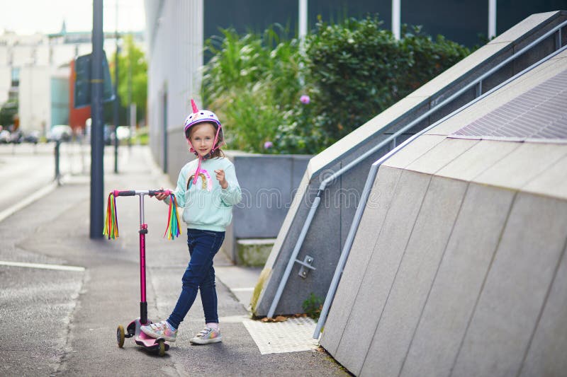 Underbart förskolelärare som rider på sin skoter i en stadspark på solvårsdag. Cute child in Unicorn-hjälmet rider en push arkivbild