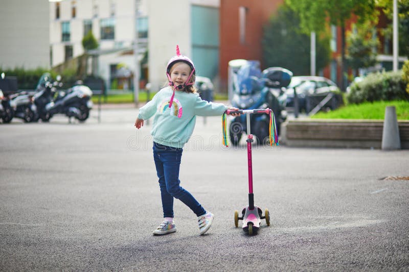 Underbart förskolelärare som rider på sin skoter i en stadspark på solvårsdag. Cute child in Unicorn-hjälmet rider en push arkivbilder