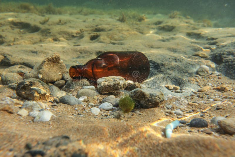 Underwater photo, discarded small beer bottle on sea floor. Ocean littering concept royalty free stock image Underwater photo, discarded small beer bottle on sea floor. Ocean littering concept royalty free stock image