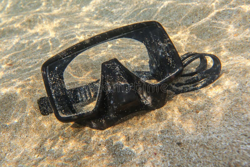 Underwater photo - sun shines on black diving mask on sand in shallow water near beach stock image Underwater photo - sun shines on black diving mask on sand in shallow water near beach stock image