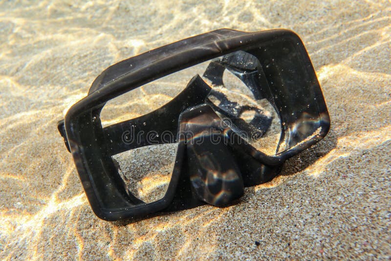 Underwater photo - sun shining to rubber black diving mask on sand in shallow water stock image Underwater photo - sun shining to rubber black diving mask on sand in shallow water stock image