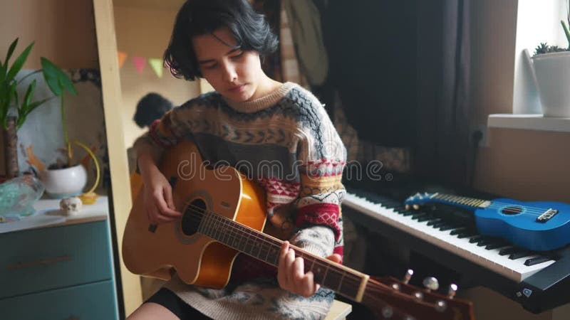Une adolescente joue de la guitare dans sa chambre. concept de rêve de musique familiale heureuse. jeune guitariste adolescente. a banque de vidéos