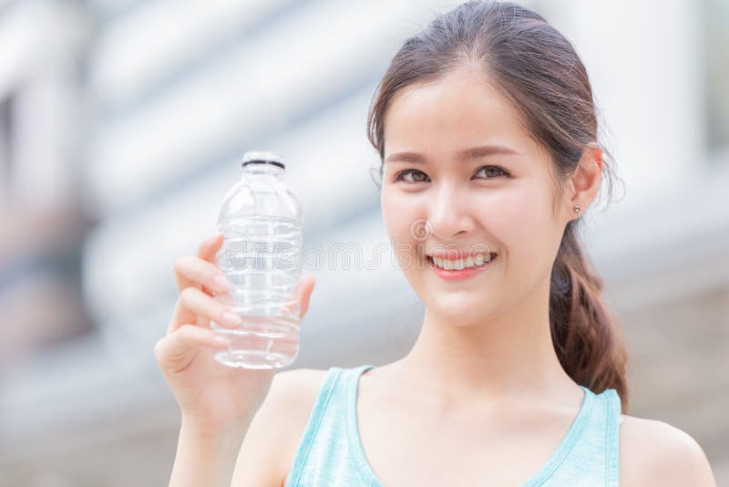 Une adolescente qui boit de l'eau joyeuse sourire en tenant une bouteille en plastique