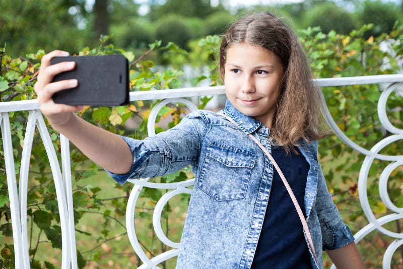 Une adolescente qui prend le selfie avec son smartphone, assise sur un banc dans un parc photos stock