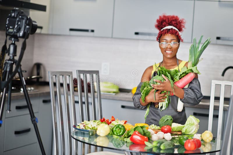 Une afro-américaine filmant son blog a diffusé un reportage sur la nourriture saine à la maison. elle tient les légumes à la main image stock