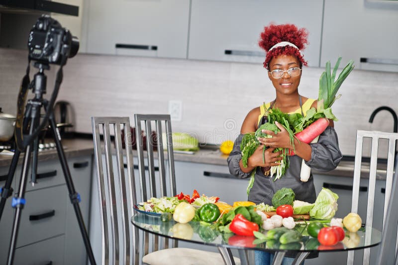 Une afro-américaine filmant son blog a diffusé un reportage sur la nourriture saine à la maison. elle tient les légumes à la main images stock
