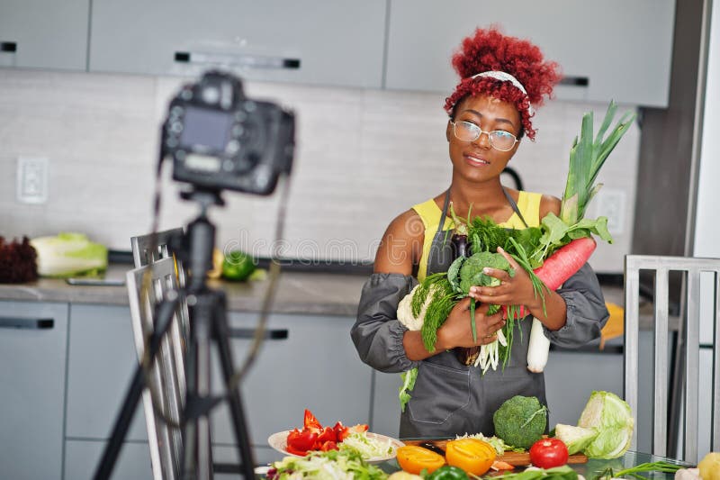 Une afro-américaine filmant son blog a diffusé un reportage sur la nourriture saine à la maison. elle tient les légumes à la main image libre de droits