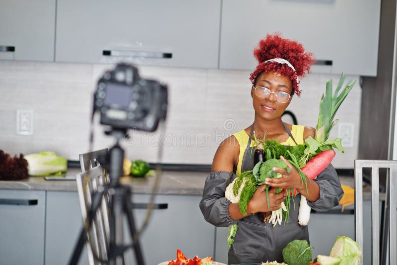 Une afro-américaine filmant son blog a diffusé un reportage sur la nourriture saine à la maison. elle tient les légumes à la main photos stock