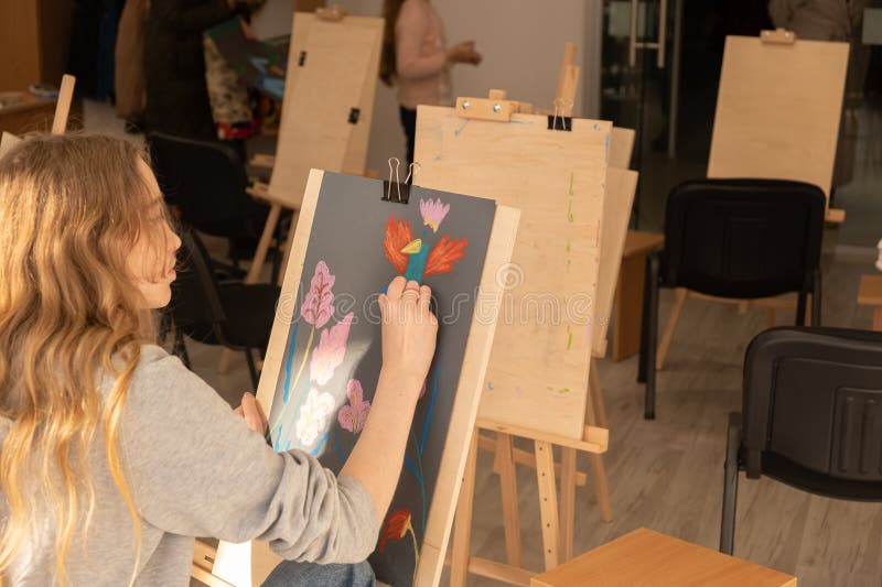 Une artiste peint une jeune fille aux cheveux longs sur une toile dans un studio ensoleillé entouré de toiles vides. image libre de droits