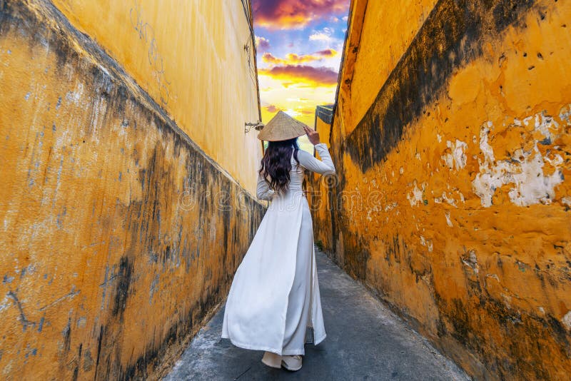 Une asiatique en costume ao dai marche dans une ruelle à hoi, une ville ancienne images libres de droits