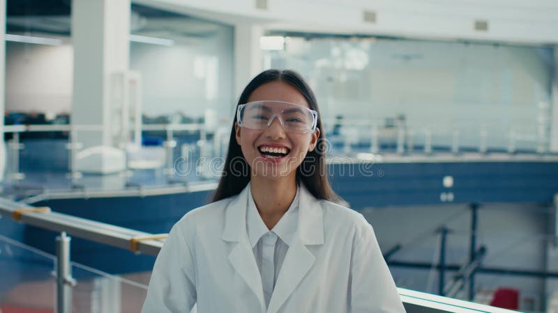 Une asiatique portant des lunettes de protection et un manteau de laboratoire riant à l'intérieur banque de vidéos
