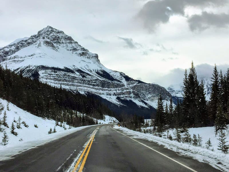 Une autoroute vide sur un paysage hivernal enneigé qui traverse les montagnes rocheuses par une belle journée d'hiver dans le par photo libre de droits Une autoroute vide sur un paysage hivernal enneigé qui traverse les montagnes rocheuses par une belle journée d'hiver dans le par photo libre de droits