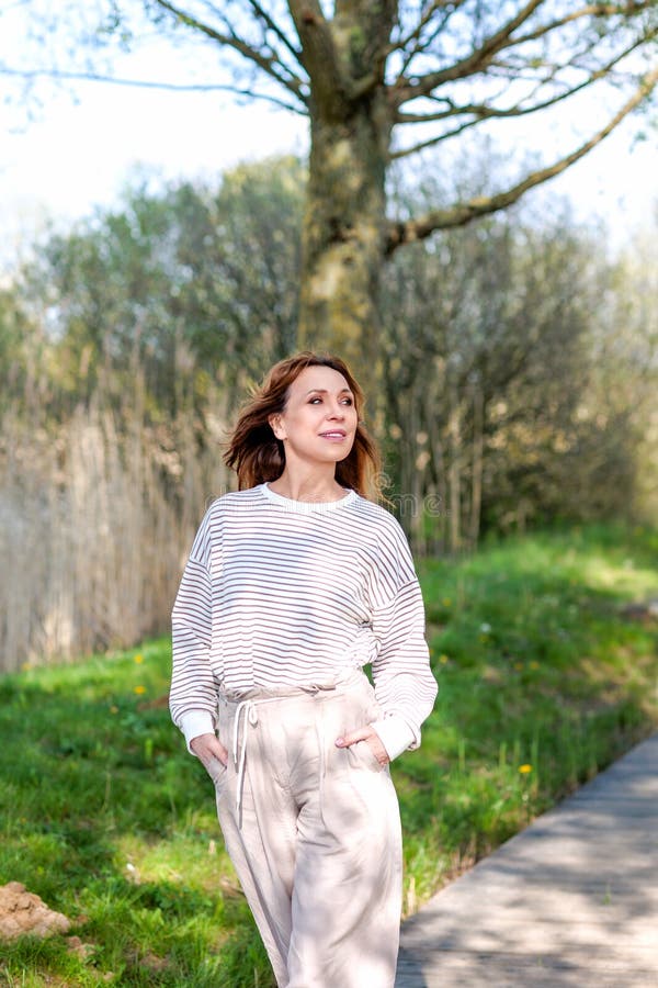 Une belle femme d'âge moyen pose dans la nature un après-midi ensoleillé de printemps. l'interaction de la lumière du soleil et des ombres des arbres crée un effet visuel.