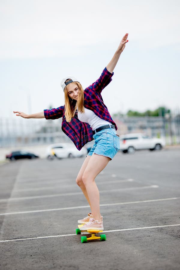 Une belle fille blonde portant les caleçons à carreaux de chemise, de chapeau et de denim longboarding tout en étirant ses mains photos libres de droits Une belle fille blonde portant les caleçons à carreaux de chemise, de chapeau et de denim longboarding tout en étirant ses mains photos libres de droits