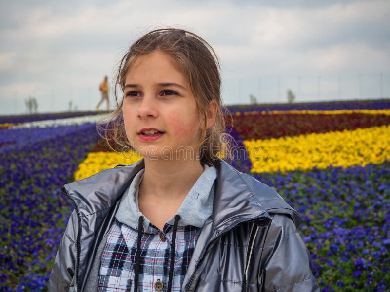 Une belle fille regarde dans la distance debout sur le fond d'un lit de fleurs multicolore. portrait d'une adolescente image stock
